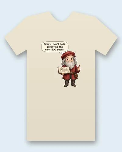 Leonardo da Vinci tee mockup: Leonardo da Vinci with a long white beard, in a red cap and tunic, holding a sketchbook full of gear and wing drawings, saying “Sorry, can't talk. Inventing the next 500 years.”