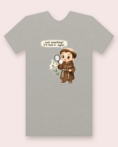 Saint Anthony of Padua tee mockup: a rosy-cheeked friar in a brown habit with a rope belt, peering through a big magnifying glass, with a book under his arm and white lilies beside him, saying “Lost something? I'll find it. Again.”