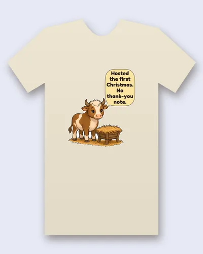 Stable Ox tee mockup: A brown and white ox with short horns standing beside a wooden manger full of hay, with a speech bubble above it, saying “Hosted the first Christmas. No thank-you note.”