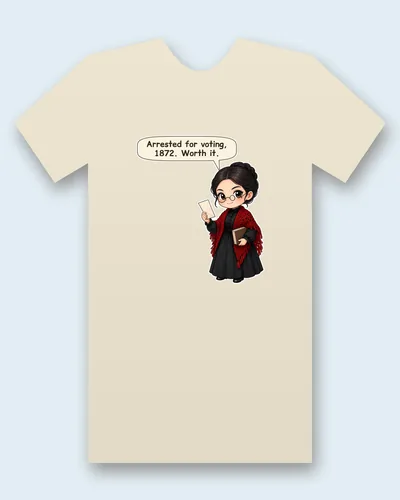 Susan B. Anthony tee mockup: Susan B. Anthony with round wire glasses and dark hair in a braided bun, a black Victorian dress and a red crocheted shawl, holding a folded paper and a book, saying “Arrested for voting, 1872. Worth it.”